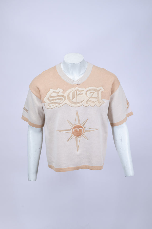 Mannequin wearing a beige and white Mediums Collective SEA 206 Knit V neck sports jersey with a SEA Velour embroidery design on a white background