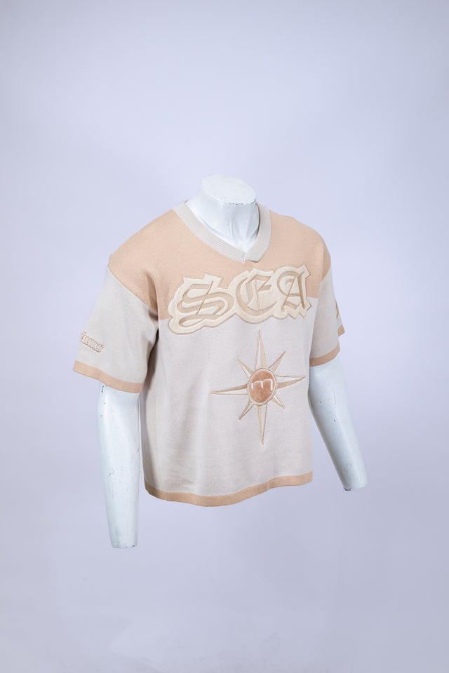 Mannequin wearing a beige and white Mediums Collective SEA 206 Knit V neck sports jersey with a SEA Velour embroidery design on a white background