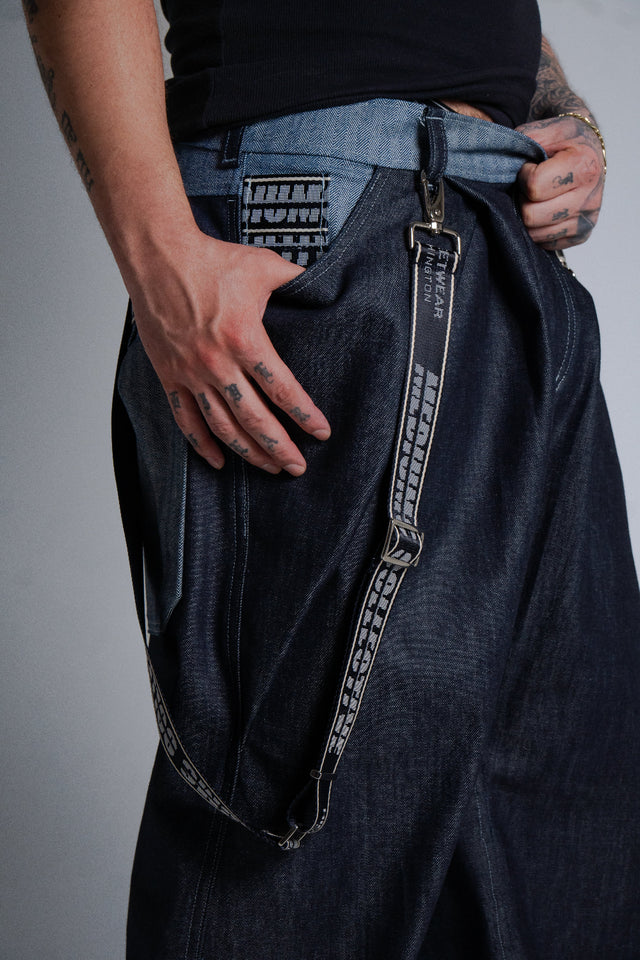 Person wearing Mediums Collective dark blue pants with a chain detail, on a plain background