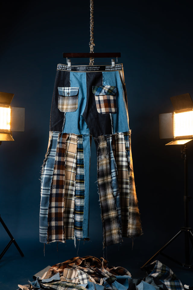 Plaid shirt and pants hanging on a stand against a dark background with studio lights.