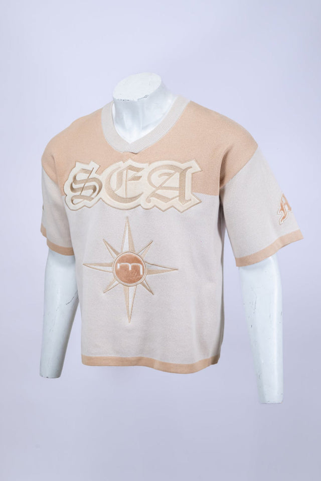 Mannequin wearing a beige and white Mediums Collective SEA 206 Knit V neck sports jersey with a SEA Velour embroidery design on a white background