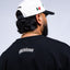 Person wearing a black t-shirt with 'Mediums' logo and a white cap with black visor and Mexican flag design.