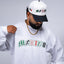 Person wearing a white long-sleeve shirt with 'MEXICO' printed on it, a white cap, and a black cap with visible branding. Mexico graphic tee, Mexico long sleeve shirt, Mexican streetwear, Latino streetwear, Mediums Collective, Seattle streetwear, Mexico shirt, Mexico soccer shirt, fútbol fashion, Mexican heritage clothing, men’s graphic tee, men’s long sleeve graphic shirt, pine green tee, black long sleeve shirt, white long sleeve shirt, cultural streetwear, World Cup outfit, Mexico capsule, Latino fashion