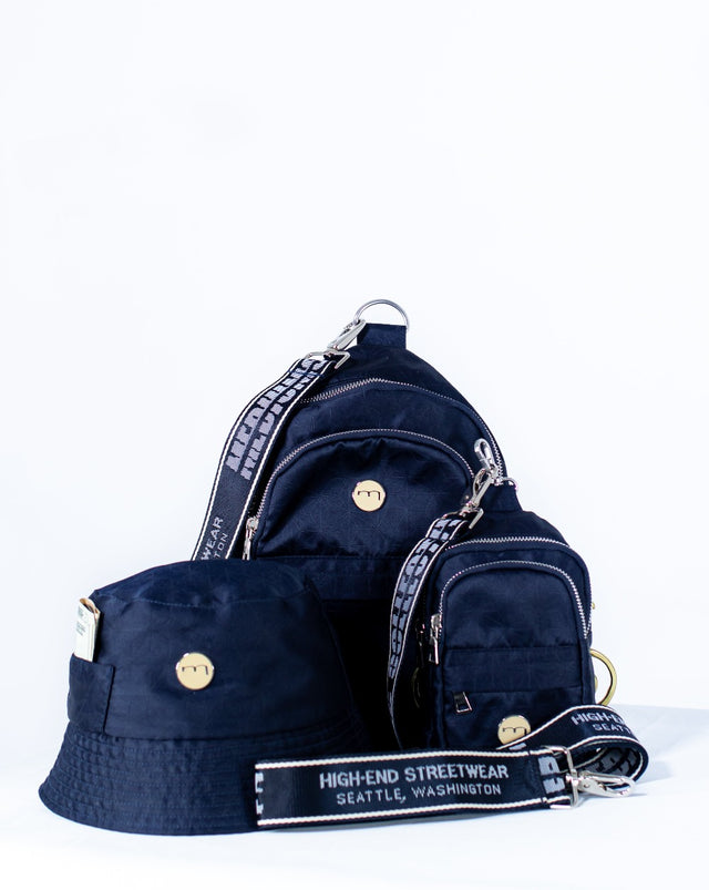 The Mediums Collective main is a super convenient, lightweight, and comfortable bag, meant for carrying you personal goods. It features our custom 22 collection fabric, an adjustable nylon belt for premium comfort on the shoulders, and multiple compartments for extra items. This is the bag that completes the fill fit. navy nylon, streetwear, bag, pack, metal buckle, bucket hat, 